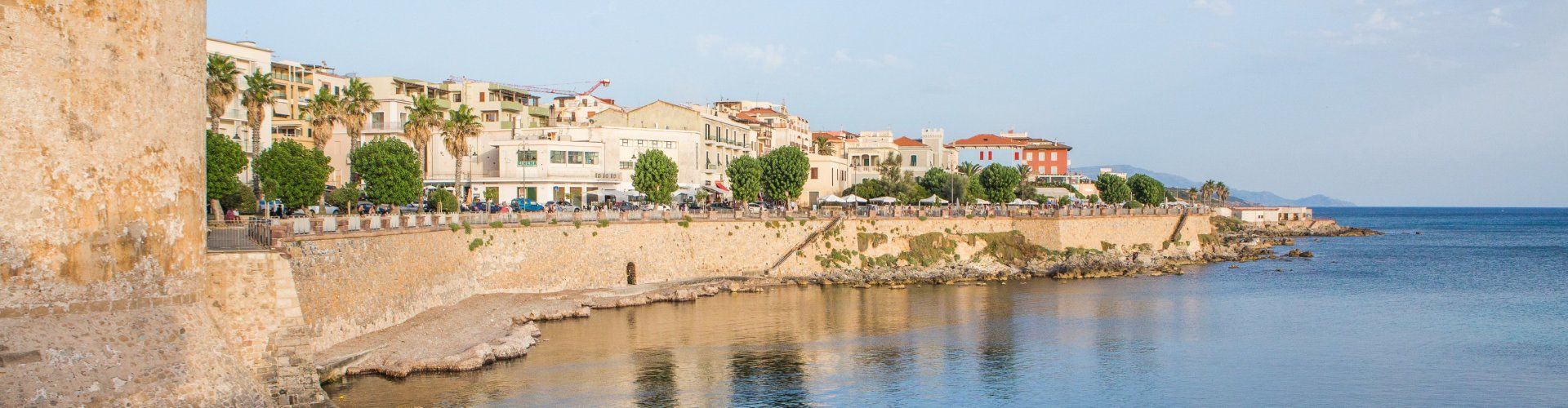 La silhouette di Alghero dietro le mura della città si specchia nel mare tranquillo