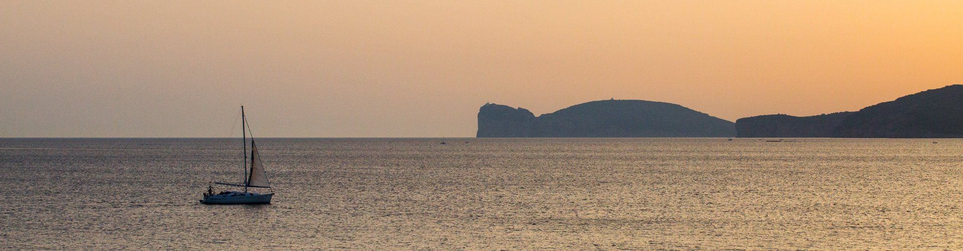 Il mare di Alghero al tramonto con una barca vela e Capo Caccia all´orizzonte