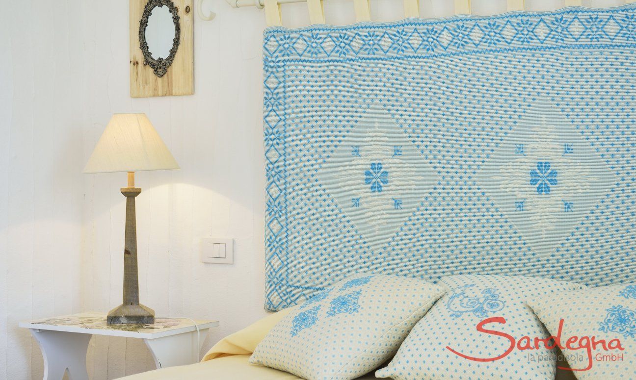 Li Conchi 7 | Camera 1 con letto matrimoniale con testata in tessuto sardo Letto matrimoniale con tavolino, lampada e testata in stile sardo in Li Conchi 7