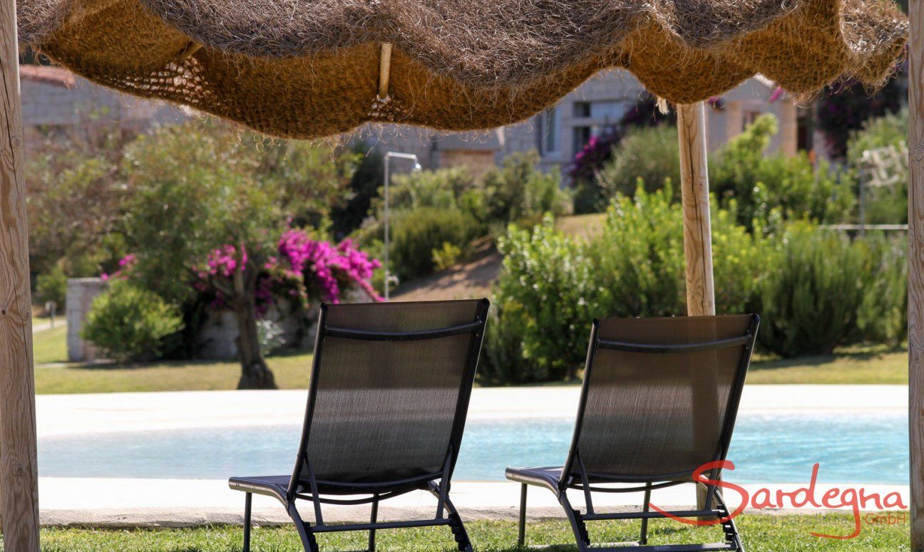 Lettini da sole sotto un ombrellone a fianco alla piscina di Li Conchi