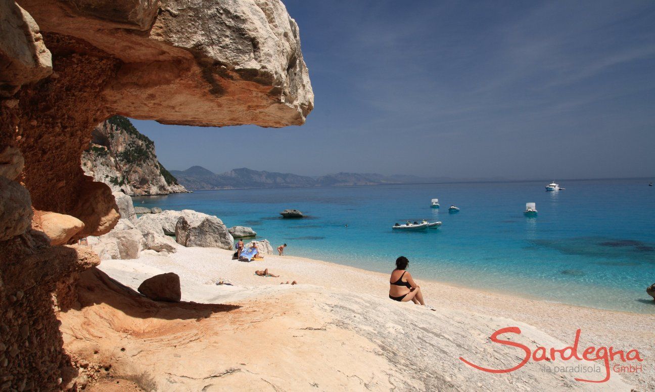 Donna seduta sulla spiaggia davanti alle rocce di Cala Luna guardando il mare e i gommoni sul mare