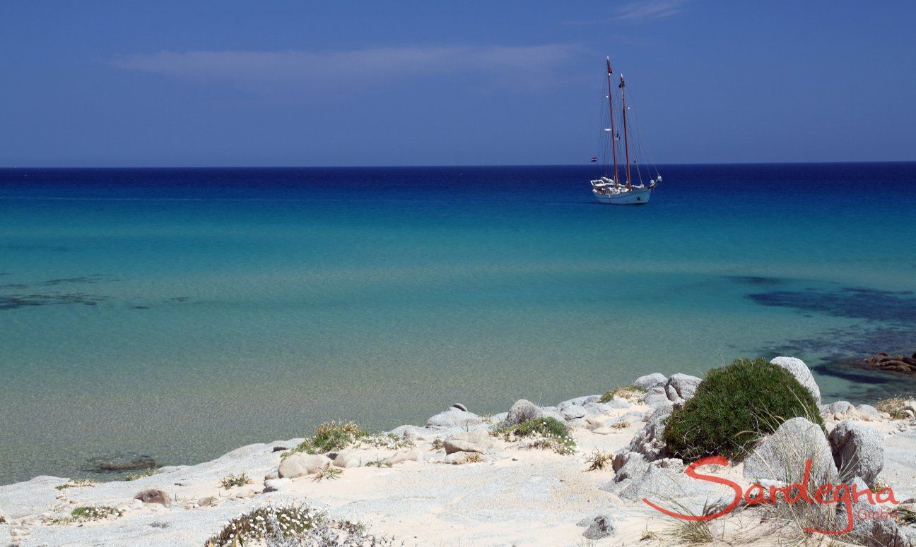 Spiaggia con mare turchese e barca a vela