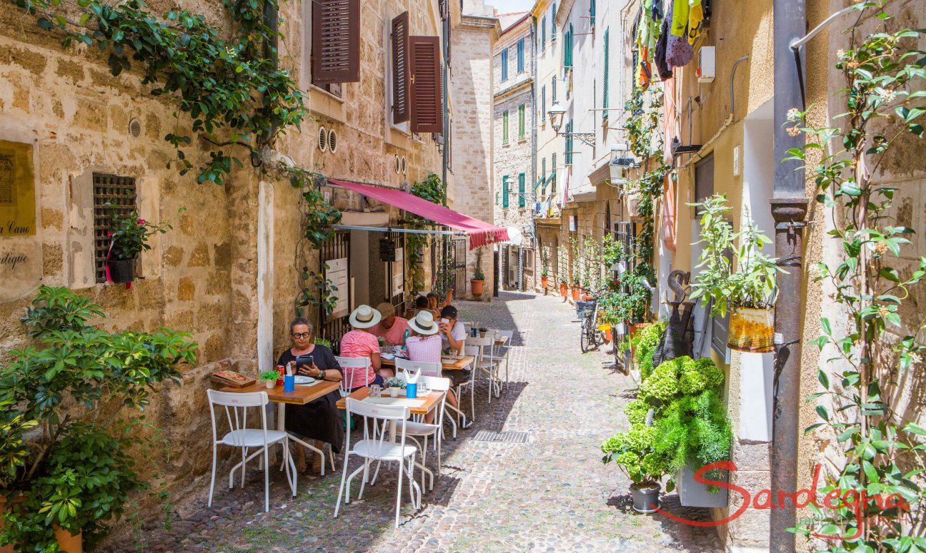 Stradina pedonale del centro storico di Alghero con tavolini di un ristorante per mangiare all'aperto