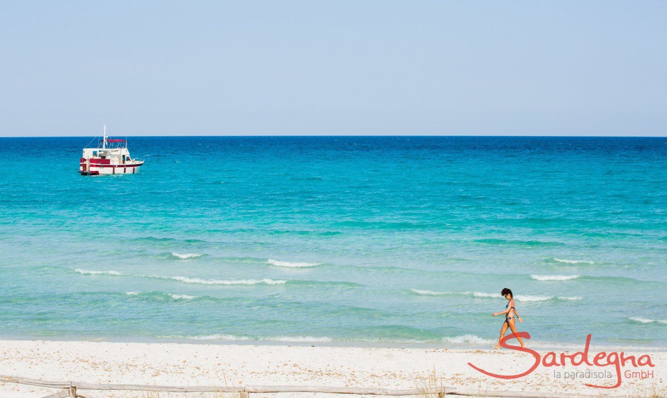 Una donna cammina sulla battiggia bianca della spiaggia La cinta davanti al mare celeste con una barca bianca e rossa