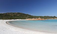 Spiaggia Romazzino fatto di sabbia bianca a forma di mezza luna, alla fine rocce giallie e una collina coperta di macchia verde