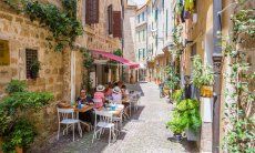 Stradina pedonale del centro storico di Alghero con tavolini di un ristorante per mangiare all'aperto