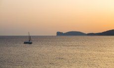 Il mare di Alghero al tramonto con una barca vela e Capo Caccia all´orizzonte