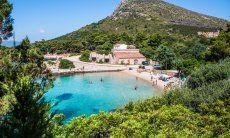 Baia di Cala Moresca con acqua limpida, spiaggia bianca e due casa in mezzo alla macchia mediterranea