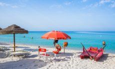 Postazione bagnino con sedia, ombrellone e pattino rosso sulla spiaggia di sabbia bianca