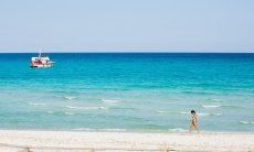 Una donna cammina sulla battiggia bianca della spiaggia La cinta davanti al mare celeste con una barca bianca e rossa