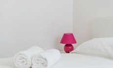 Villa Pola | Letto bianco con asciugamani e abat-jour fuchsia Letto bianco con asciugamani e abat-jour fuchsia